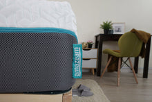 Load image into Gallery viewer, Side view of the Amazeam mattress displaying the logo tag, 4D side cover with a honeycomb design for airflow, and a turquoise zipper. The chill fabric top cover is visible, with a blurred background featuring a chair, desk, low cabinet, fluffy slippers, a mat, and a gold clock, adding a touch of elegance and comfort to the setting