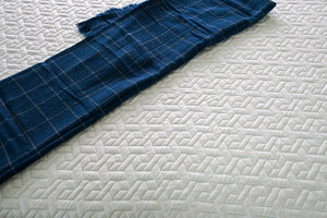 Mattress with a 'ketupat'-inspired quilted design, reminiscent of Malaysian rattan weaving, featuring a fabric that is cool to the touch, complemented by a navy blue blanket, blending cultural artistry with comfort